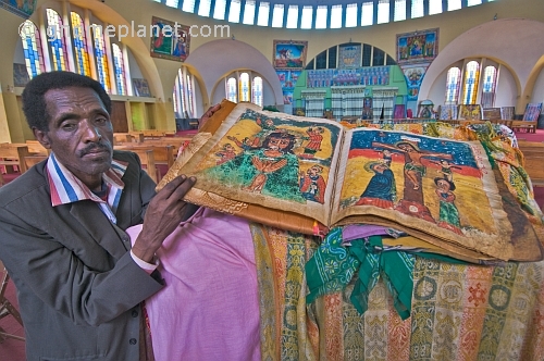 caption: Church warden holds an illustrated vellum Bible in the new church of 'St Mary of Zion'.