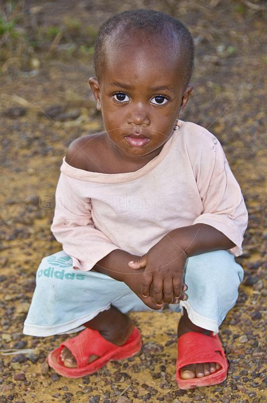 Young Gabonese girl with short hair in a light pink shirt and red shoes.