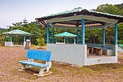 Three covered picnic areas and a blue bench by the side of the road.