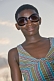 Image of Gabonese teenager with short hair and sunglasses wears a striped dress.