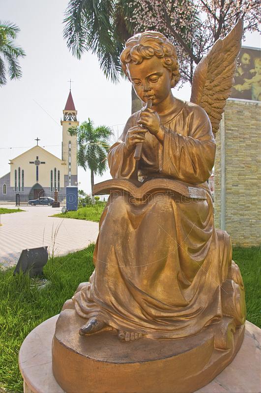Golden statue of angel playing music in front of the white stucco Roman Catholic church.