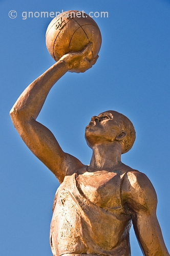 Bronze painted statue of footballer holding a ball above his head.