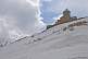 Image of Snow-covered mountains contrast the bare stone of the Tsminda Sameba Monastery.