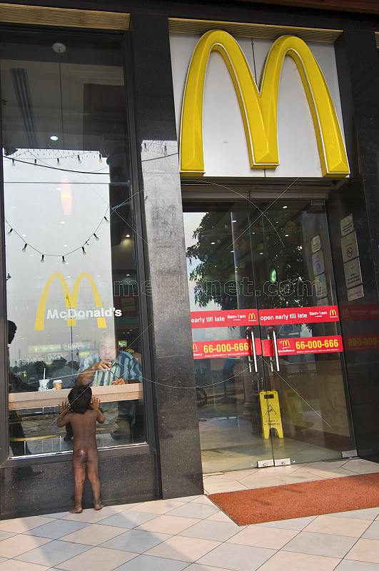 A naked beggar-girl waits hungrily outside a McDonalds restaurant on Connaught Place.