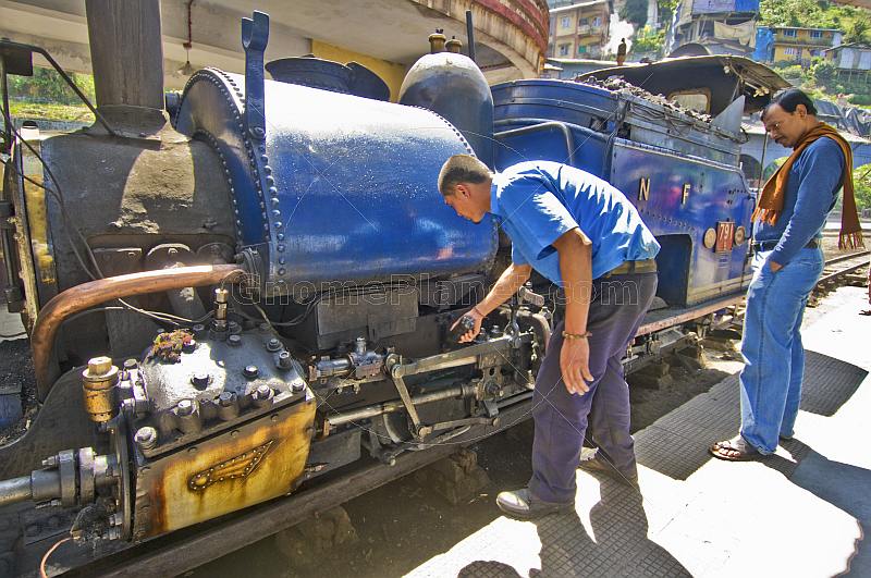 A passenger watches the engineer make adjustments to a steam locomotive on the Darjeeling Himalayan Railway.