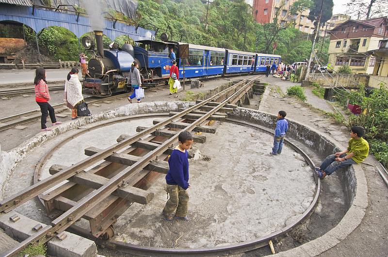Three boys play on the narrow gauge turntable as a steam train on the Himalayan Mountain Railway approaches Darjeeling Station.