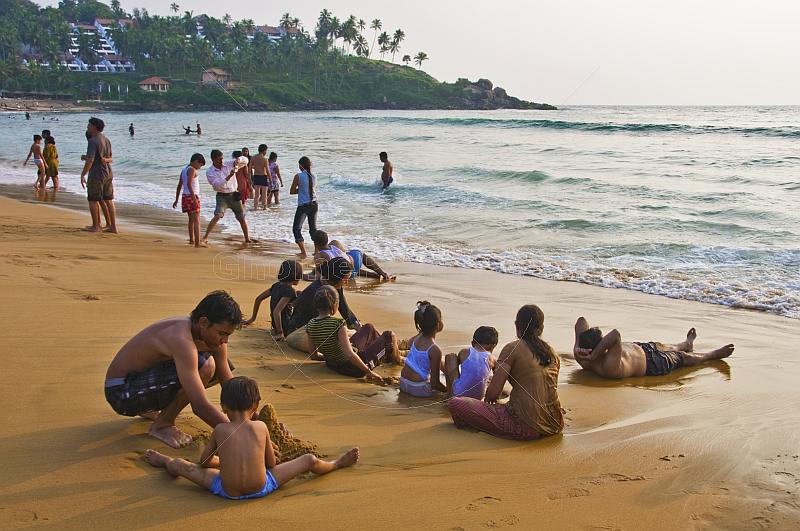 Indian families play in the waves on Leela Beach at sunset.