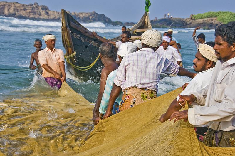 Fishermen struggle to haul their fishing net through the surf.