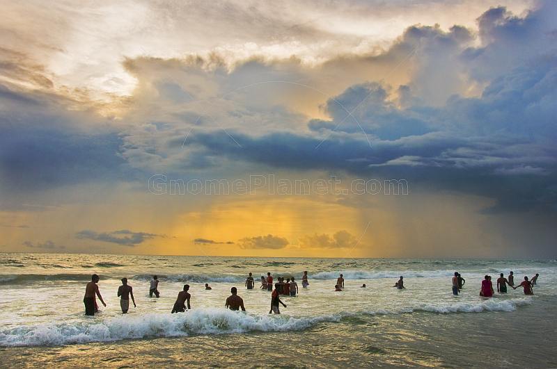 Indian bathers play in the surf during a cloudy sunset.