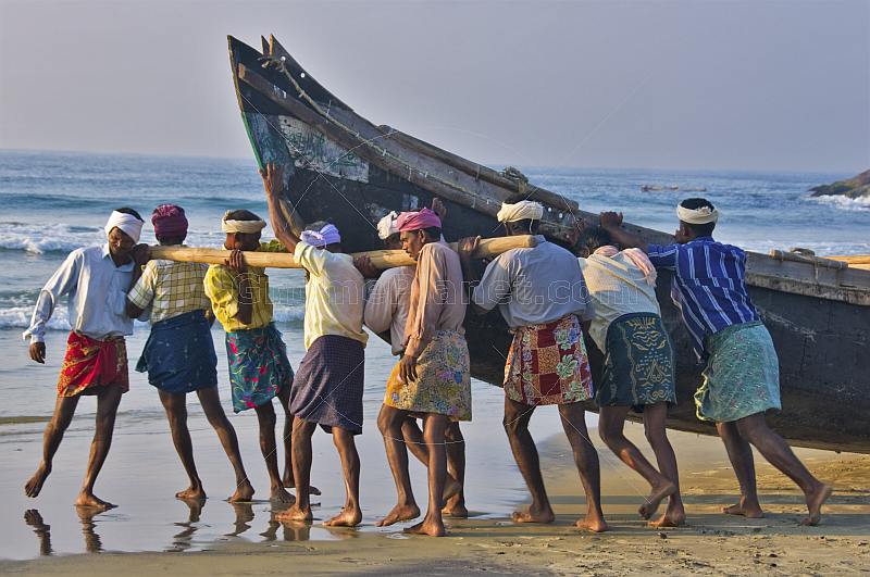 Fishermen strain to launch their fishing boat into the surf.