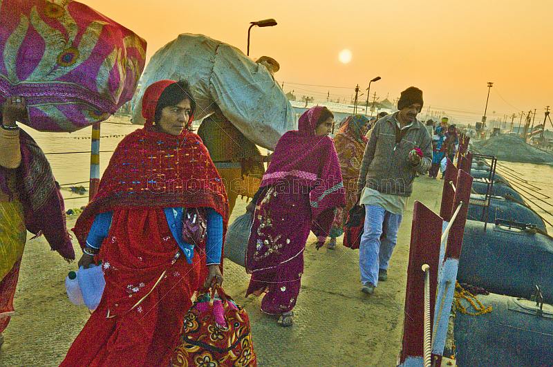 Pilgrims cross Ganges river pontoon bridge at dawn to join Kumbh Mela festival.