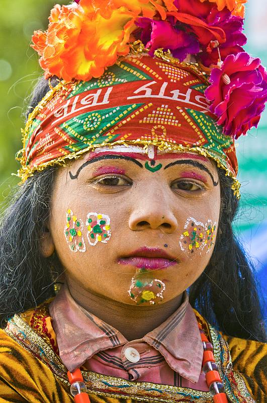 Girl with face paint and flower filled turban raises money from Kumbh Mela pilgrim visitors.