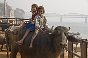 Indian girl and boy riding a buffalo, on the banks of the Ganga River.