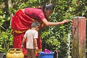 caption: A small Indian boy waits for his mother to give him a bucket bath.