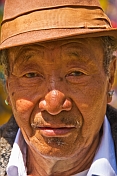 Elderly Buddhist man in hat and earing.