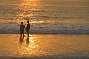 Young Indian couple hold hands in the surf at sunset.