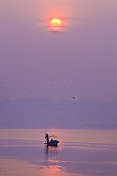 Solitary rowing boat with pilgrim visits Sangam on River Ganges in early dawn light.