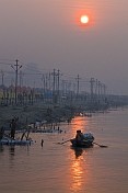 Solitary rowing boat passes bathing pilgrims on River Ganges in early dawn light.