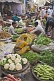Image of Traders at a busy vegetable markets squat to sell fruit, vegetables, herbs, and fresh spices.