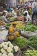 Image of Traders at a busy vegetable markets squat to sell fruit, vegetables, herbs, and fresh spices.