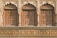 Three ancient brown wooden doors set in carved sandstone frames.