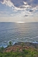 Image of Sunlight illuminates a patch of sea off the palm-tree lined coast.