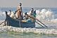 Image of Fishermen battle the waves to launch their boat at Kovalam Beach.