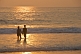 Image of Young Indian couple hold hands in the surf at sunset.