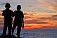 Young Indian couple watch the sunset from rocks above Hawa Beach.