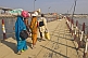 Image of Barefoot village pilgrims carry belongings on head to cross Ganges River pontoon bridge.