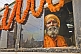 Elderly saffron-clad Hindu Holy Man looks from decorated bus window.