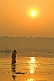 Image of Woman in sari walks through Ganges River shallows at dawn for a ritual bath.