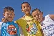 Three Kazakh boys pose for a photo in bright sunshine near the Aral sea.