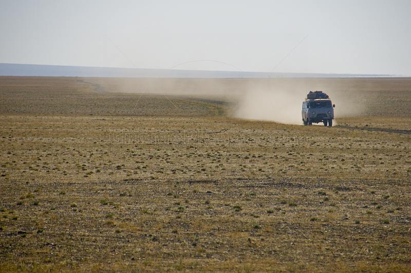 Mongolian minibus raising a dust cloud as it crosses the arid Gobi desert landscape.