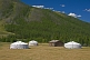 A group of yurts and a log cabin nestle in a forested mountain valley.