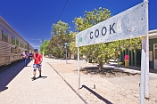 Passengers from Indian Pacific train walk past Cook railway station signboard.