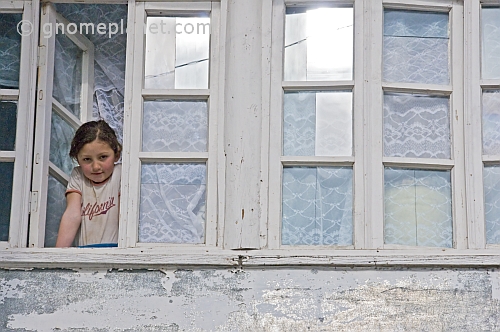 A young girl in a California teeshirt looks out of the window of her village house.