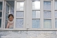 A young girl in a California teeshirt looks out of the window of her village house.
