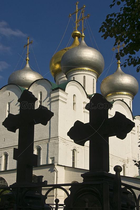 The sharp black silhouettes of two tombstones in the shape of crosses contrast the gold crosses on the Smolensk cathedral at the Novodevichy Convent.