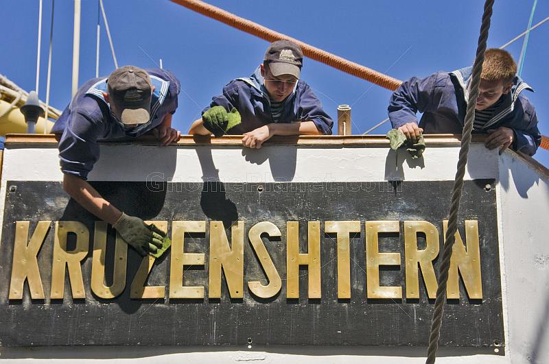 Young Russian cadets clean the brass nameplate of the sailing ship 'Kruzenshtern'.
