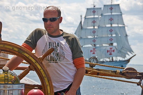 Man at the wheel of the 3 masted barque 'Picton Castle' with tallship 'Sagres' in background.