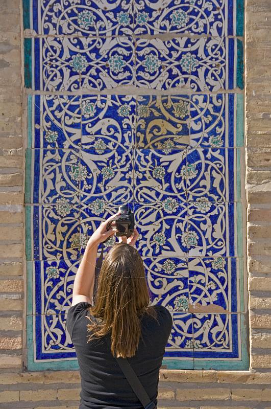 Tourist woman photographs some blue glazed ceramic tilework on the Mohammed Amin Khan Medressa.