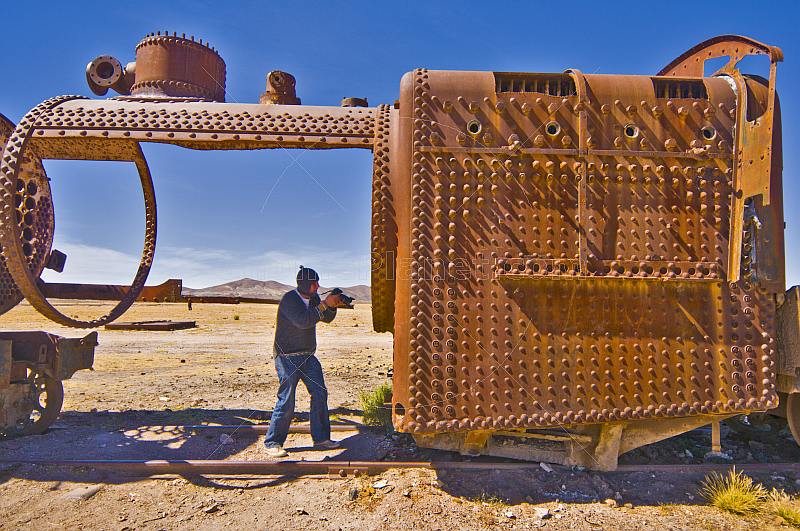 Man photographs rusting steam locomotive in the cemetery of steam engines.