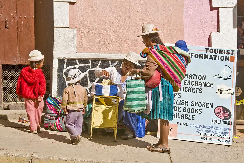 Traditionally dressed Bolivian woman with children buys maize snack from street vendor.