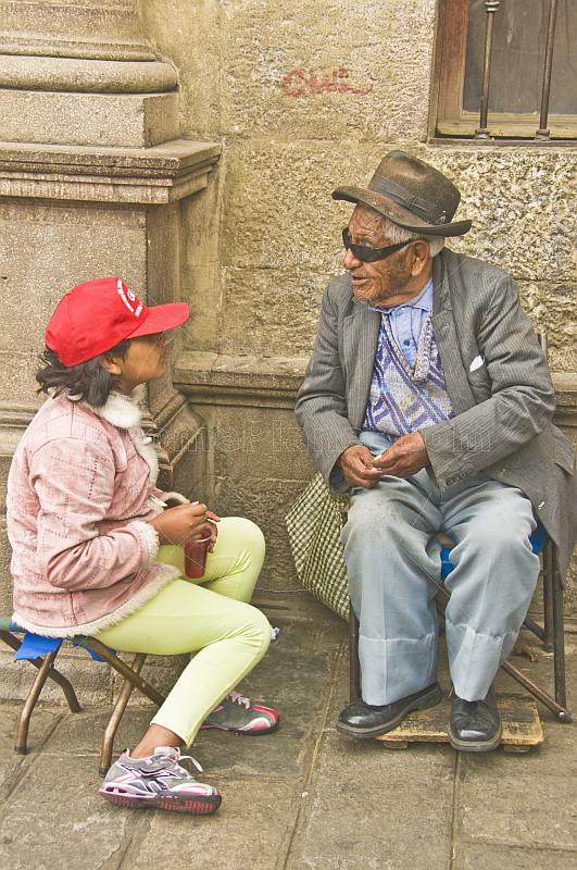 Old man talks to young girl in a red hat.