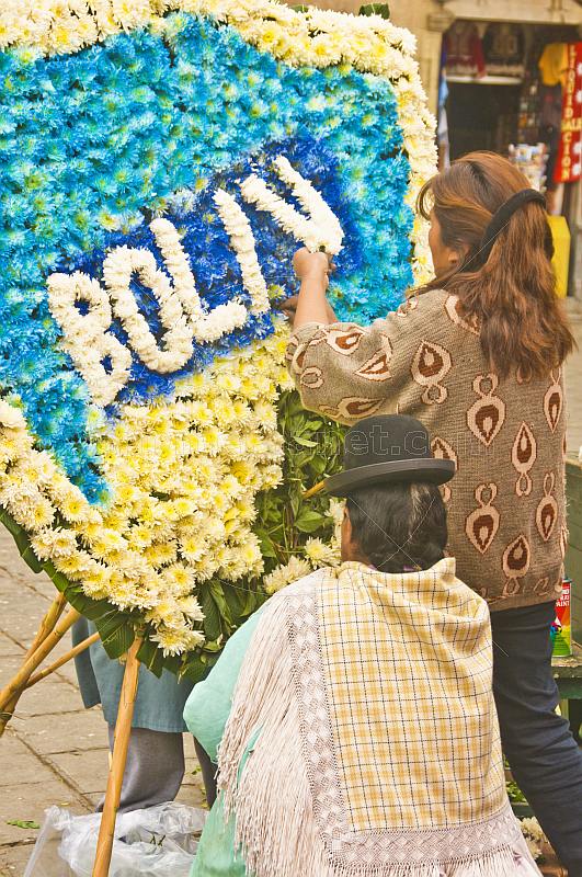 Two women work on a blue white and yellow floral shield.