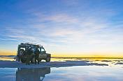 Couple with Land Rover watch the sunset over the Uyuni Salt Flats.