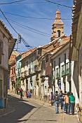 Shoppers walk along Bustillos Street with old colonial houses.