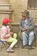 Old man talks to young girl in a red hat.