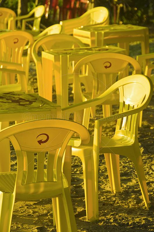 Yellow plastic chairs and tables on the beach.